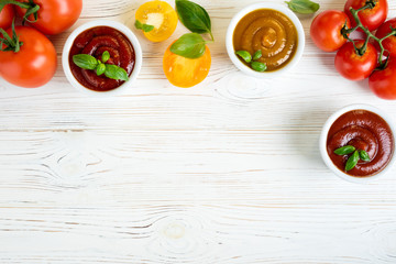 Tomato ketchup sauce in a bowls with basil and tomatoes on white wooden table. Different kinds of ketchup. Top view. Copy space