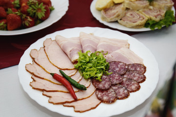 Slices of bacon lie on a plate. Assorted meat. Snacks on the festive table.