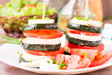 Close-up of ready-to-eat appetizer from fried zucchini, fresh tomatoes and feta cheese on a wooden skewer on a plate