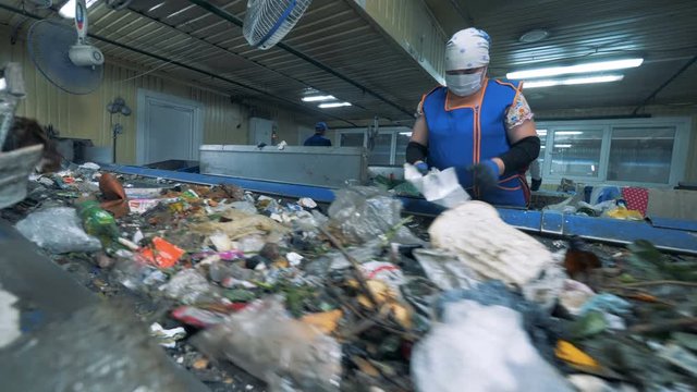 Female factory employee is sorting waste for further recycling. Waste recycling plant.