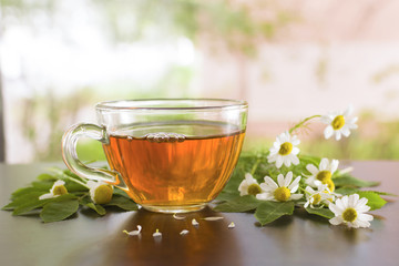 A transparent mug with tea on the table. Flowers of white daisy. Light background