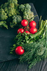 On a dark wooden table, fresh green broccoli, parsley, dill and cherry tomatoes for your health. Recipe. Ingredients. Dietary food. Place under the text. Top view.