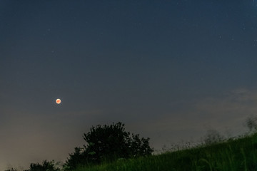 eclipsed red moon in a dark sky full of stars with planet mars