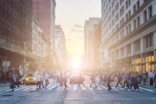 Anonymous crowd of people cross the intersection on a busy New York City street in Manhattan with sunlight background