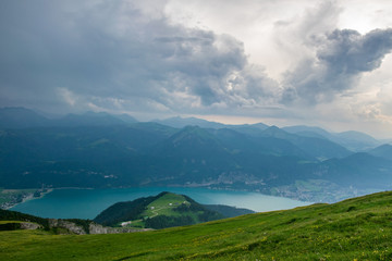 View from top of a mountain in austria with clouds on the sky and mountains and a lake in the valley