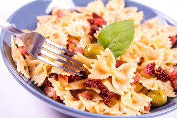 Farfalle pasta with sun dried tomato, ham and olives decorated with fresh mint eaten with a fork