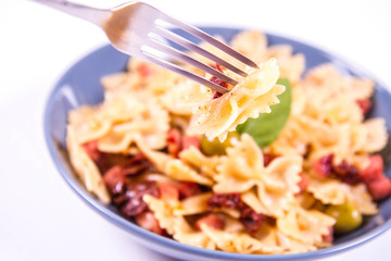 Farfalle pasta with sun dried tomato, ham and olives decorated with fresh mint eaten with a fork