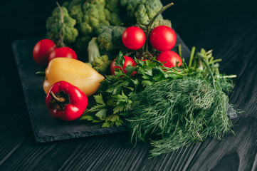 Fresh vegetables: cherry tomatoes, broccoli, pepper, dill, parsley on a dark wooden table. Recipe. Ingredients. Dietary food. Place under the text. View from above.