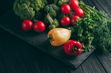 Fresh vegetables: cherry tomatoes, broccoli, pepper, dill, parsley on a dark wooden table. Recipe. Ingredients. Dietary food. Place under the text. View from above.