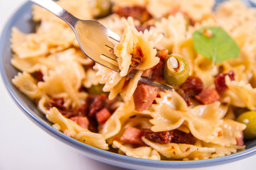Farfalle pasta with sun dried tomato, ham and olives decorated with fresh mint eaten with a fork