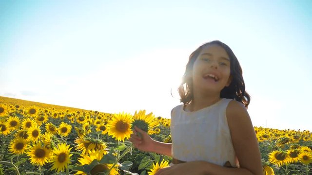 Happy little girl running happy free across the field with sunflowers. slow motion video. smelling big sunflower on summer field. Delight of a pleasant smell. Summer holiday. concept happiness
