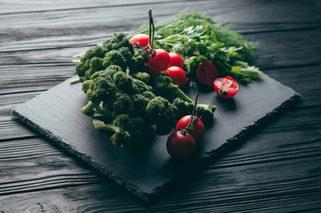 On a dark wooden table, fresh green broccoli, parsley, dill and cherry tomatoes for your health. Recipe. Ingredients. Dietary food. Place under the text. Top view.