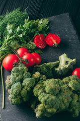 On a dark wooden table, fresh green broccoli, parsley, dill and cherry tomatoes for your health. Recipe. Ingredients. Dietary food. Place under the text. Top view.