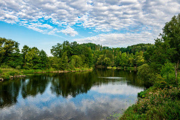 Fototapeta na wymiar River with reflection of the clouds in the water and trees behind in the bavarian forest