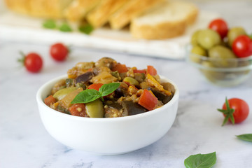 Caponata or ratatouille from a variety of vegetables served with ciabatta and olive.