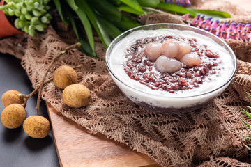 Close up soft sweet purple sticky rice pudding, Black Glutinous Rice, with longan and coconut cream on wooden table