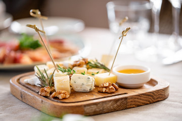Cheese plate. Delicious cheese mix with walnuts, honey on wooden table. Tasting dish on a wooden plate. Food for wine. - Powered by Adobe