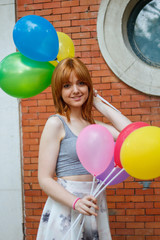 Young woman with colorful balloons on a brick wall background. 