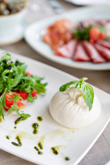 Italian Caprese salad. burrata cheese, tomatoes and basil herb leaves. Balsamic vinegar arranged on white plate