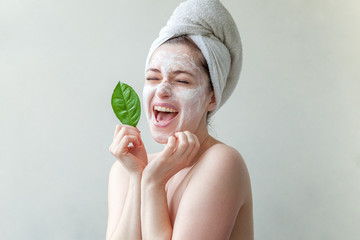 Beauty portrait of a smiling brunette woman in a towel on the head with white nourishing mask or...