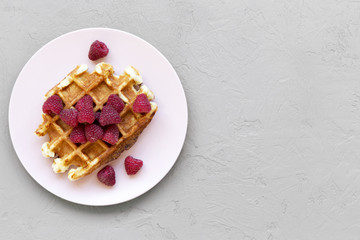 Traditional belgian waffle with raspberries on pink plate over concrete background, view from above. Copy space.
