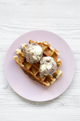 Traditional belgian waffle with lemon-chocolate icecream on pink plate over white wooden background, top view. Flat lay, overhead, from above.