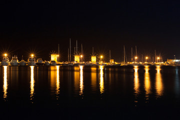 Fototapeta na wymiar Night photo of ancient fortress and pier in Rhodes city on Rhodes island, Dodecanese, Greece. Stone walls and bright night lights. Famous tourist destination in South Europe