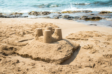 Sand castle with four towers on beach with sea in the background.