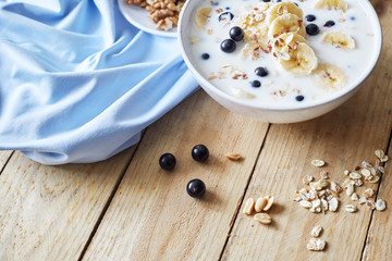 Oatmeal porridgewith bananas, nuts, raisins, blueberries and milk on table on wooden  background.  Healthy breakfast and diet food.