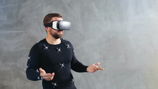 business sport man in virtual reality glasses and motion-capture suit talking to invisible partner and gesturing with hands serious calm face emotions professional movie animator negotiation skills