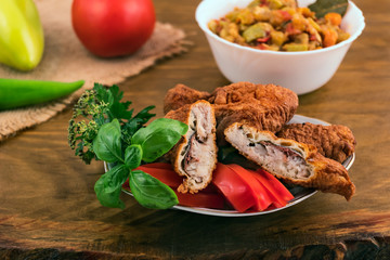 Fish in dough, deep-fried, one piece cut in half, in a plate with tomatoes, basil and parsley on the background of vegetable stew in a white plate.