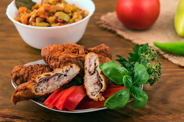 Fish in batter, fried in oil,one piece cut into two parts, in a plate with basil, parsley and sliced tomato.