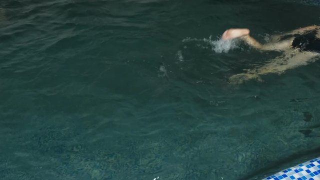 Woman is swimming in pool. Back view. Legs close-up.
