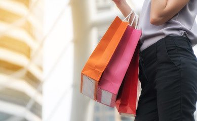 Hand of woman carrying shopping bags on city background. happiness, consumerism, sale and people concept.