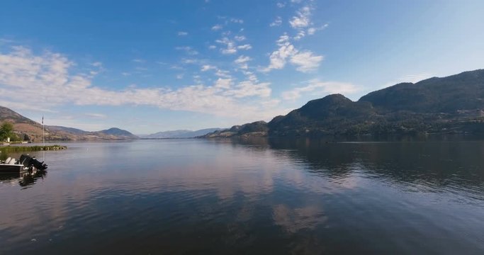 Early morning low aerial drone passing by parked boat on still water lake. Amazing background with large rocky mountains and clear blue waters in Beautiful British Columbia.