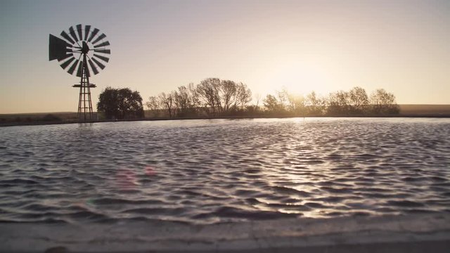Sun sets with old farm / ranch windmill spinning in the wind and reservoir full of water.