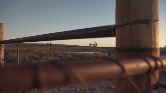 Looking through farm gate at old fashioned water pumping windmill and reservoir at sundown.