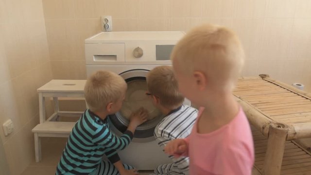 Parents bought new washing machine of new model latest generation. Children try to turn it on and wash soft toys. Three Happy boys are playing at home. Social assistance to large families.