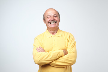 Charming handsome senior man in casual clothes keeping arms crossed and laughing