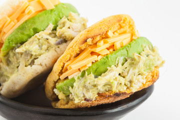 Arepas filled with shredded chicken and avocado served in a black ceramic dish on white background