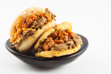 Arepas filled with shredded beef and pork rind served in a black ceramic dish on white background