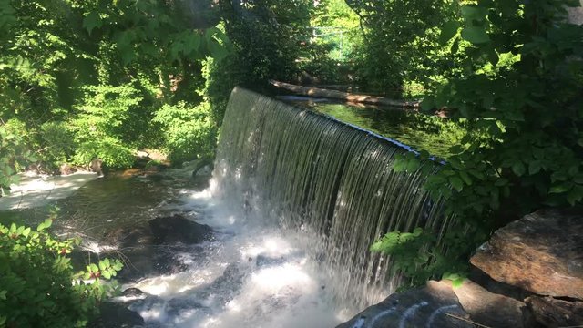 One of the many scenic waterfalls located near Sanford, Maine. A steady flow of water crashes down on the rocks below as green leaves blow in a summer breeze.