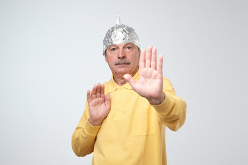 Caucasian mature man in a tin foil hat displeased closing his face with hands.