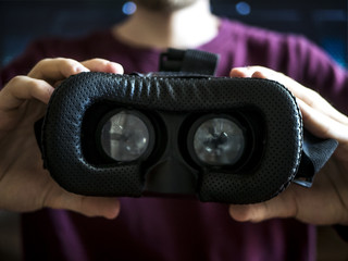 close up person holds virtual reality eye glass in front of ches on dark background