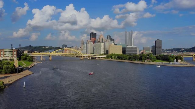 A slow rising aerial establishing shot of the skyline of Pittsburgh, Pennsylvania on an early summer evening. Ducky tour boats in the river.  	