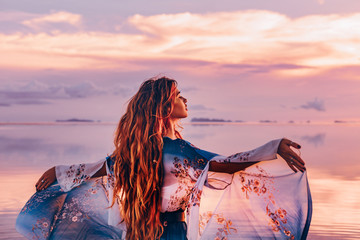 Fototapeta premium piękna młoda kobieta w eleganckiej sukni na plaży o zachodzie słońca