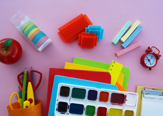 The schoolboy's accessories lie on a pink table. Textbooks and office.