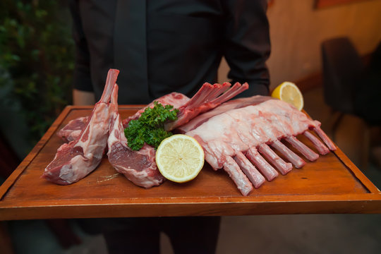 Raw lamb meat on disc wooden holding on hands of waiter in restaurant for showing. blur background.