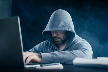 mysterious man with a beard doing something illegal on a laptop in the dark