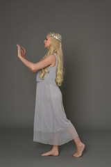 full length portrait of blonde girl wearing crow and grey dress, standing pose in side profile.  grey studio background.